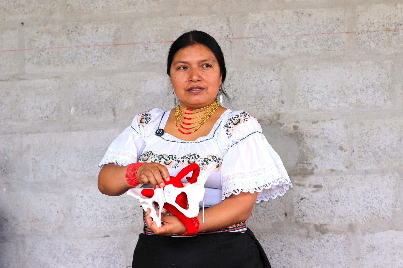 Martha Arotingo in traditional Kichwa dress holding an anatomical model of the pelvis