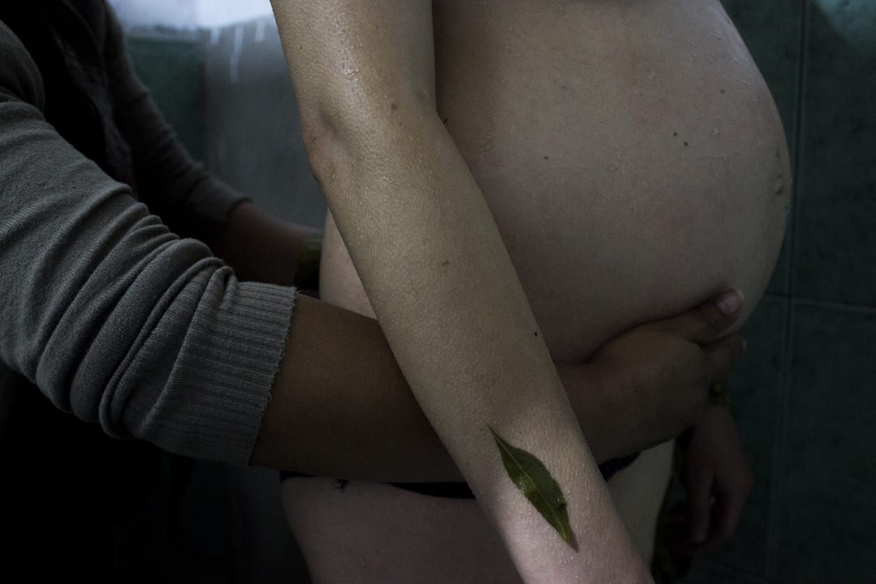 A midwife's arm around a pregnant belly, a single leaf resting on the skin